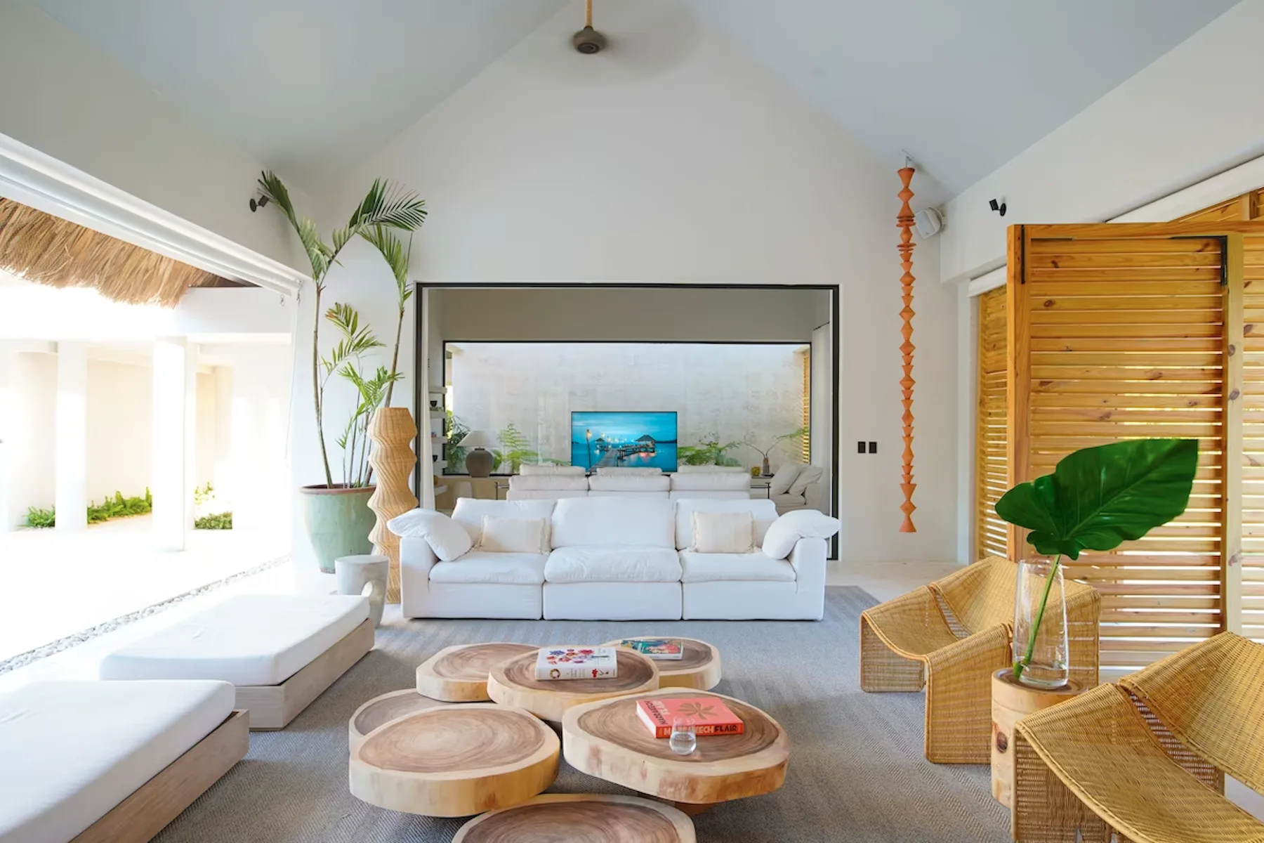 A bright living room with white seating, low tables, and tropical plants.
