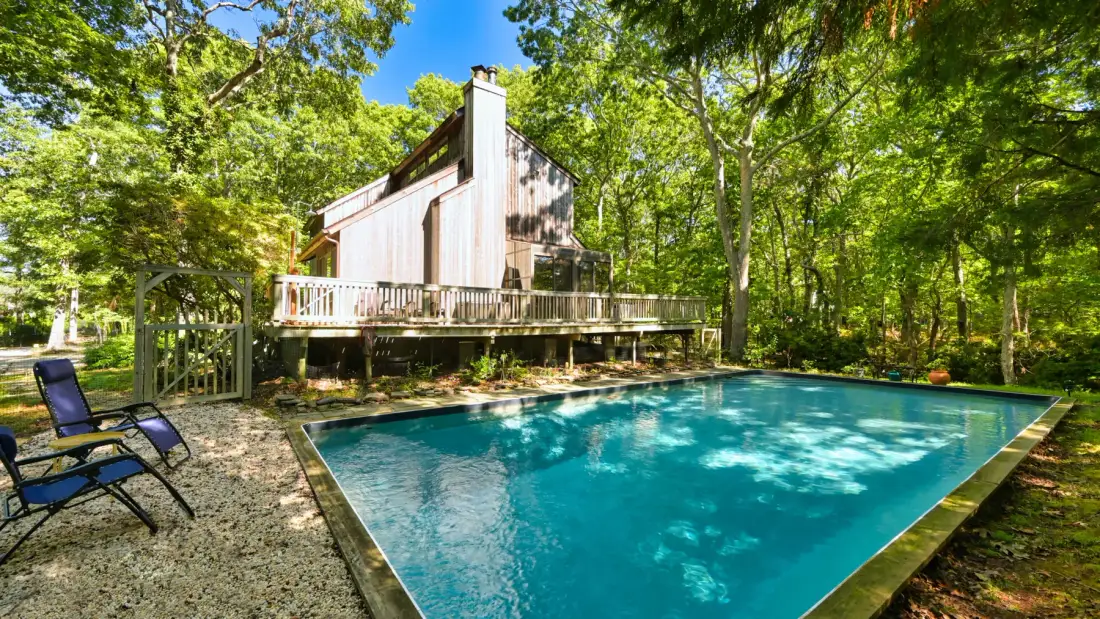 A swimming pool sits beside a raised cabin surrounded by trees.