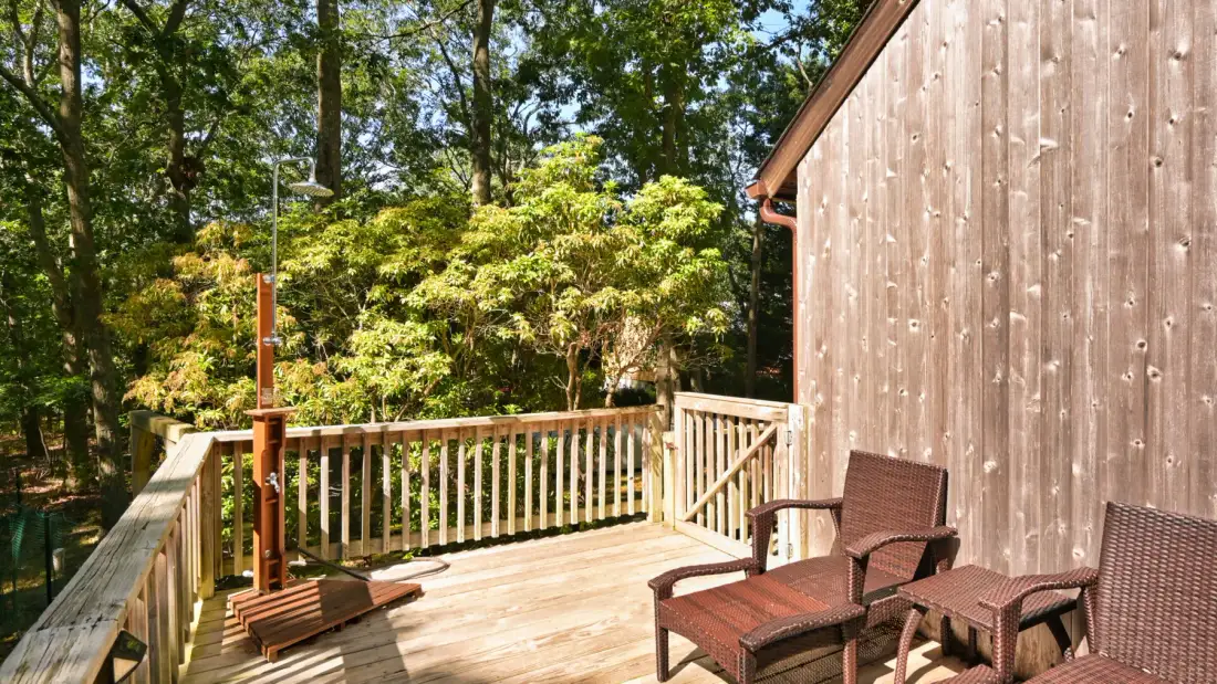 A wooden deck with outdoor seating overlooks leafy trees.