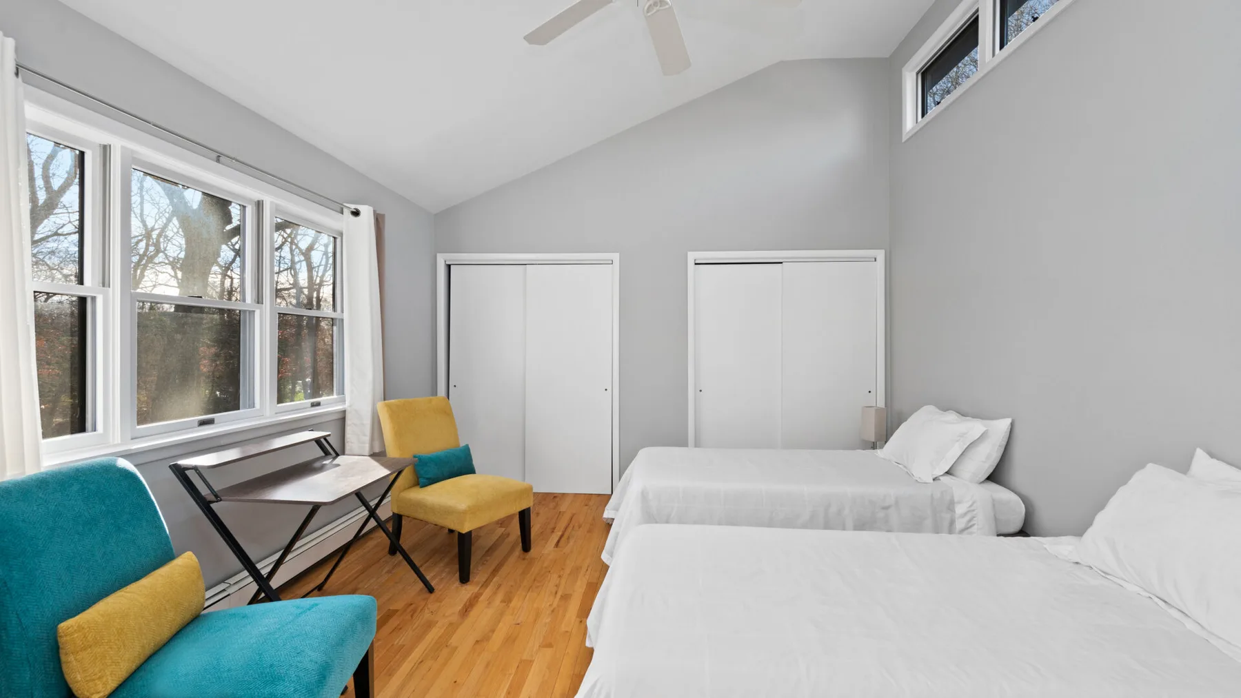 A bright bedroom with beds, a small table, and a large window.