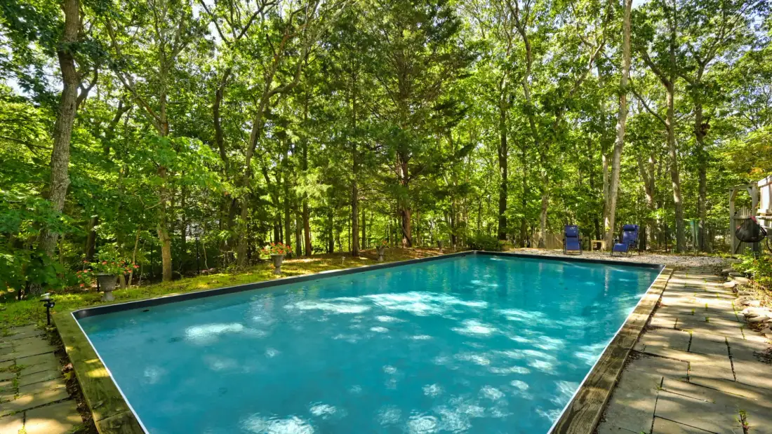 An outdoor swimming pool is surrounded by trees and paved paths.