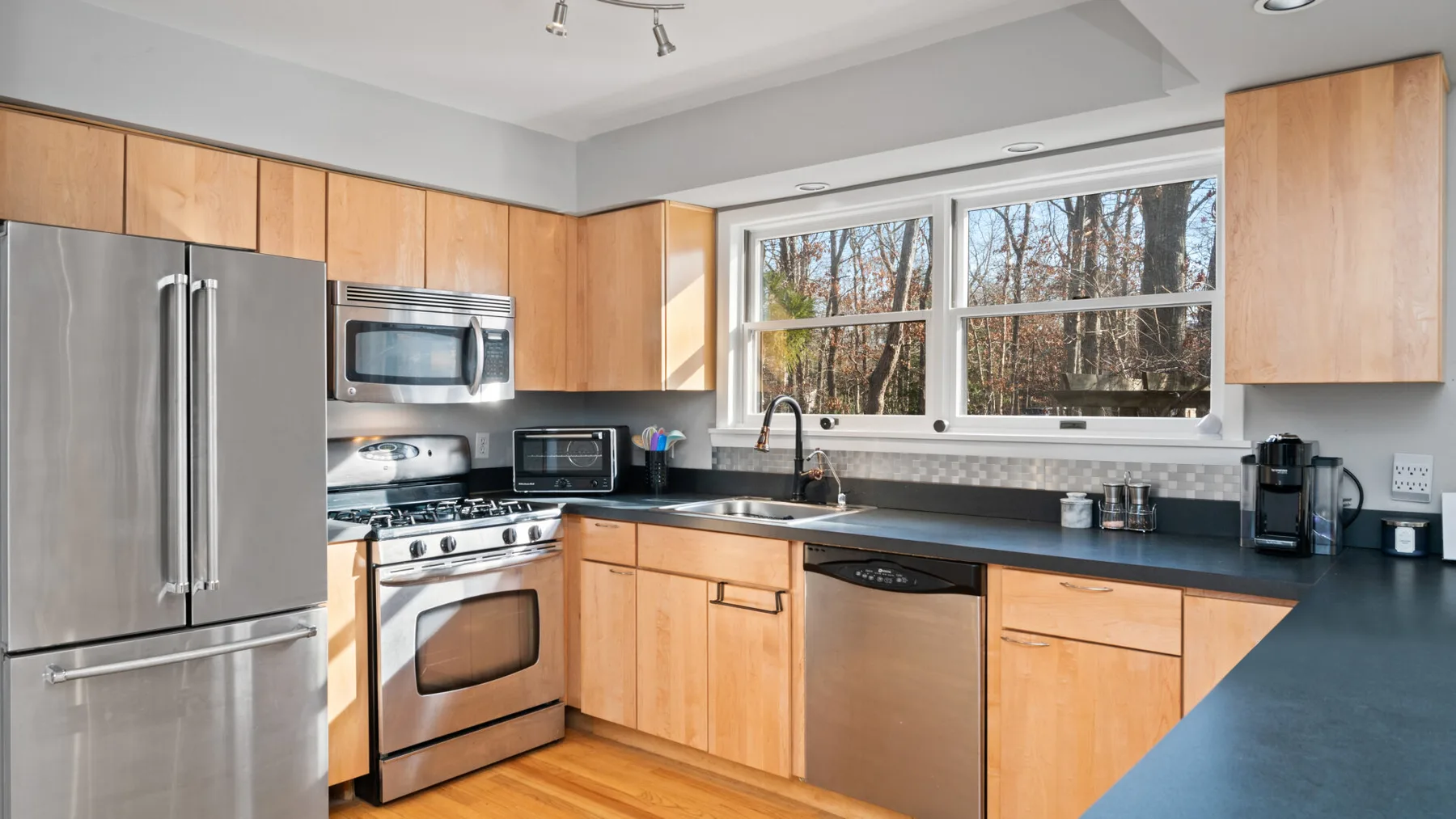 A bright kitchen with wood cabinets, stainless steel appliances, and a wide window.