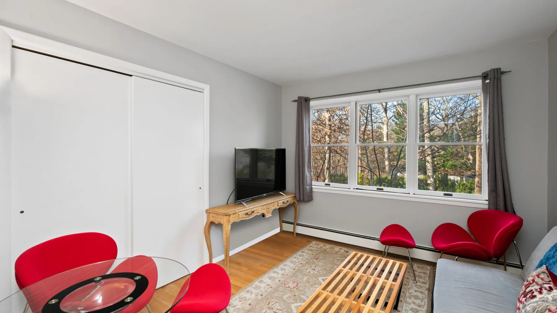A bright living room with red seating, a television, and a large window.