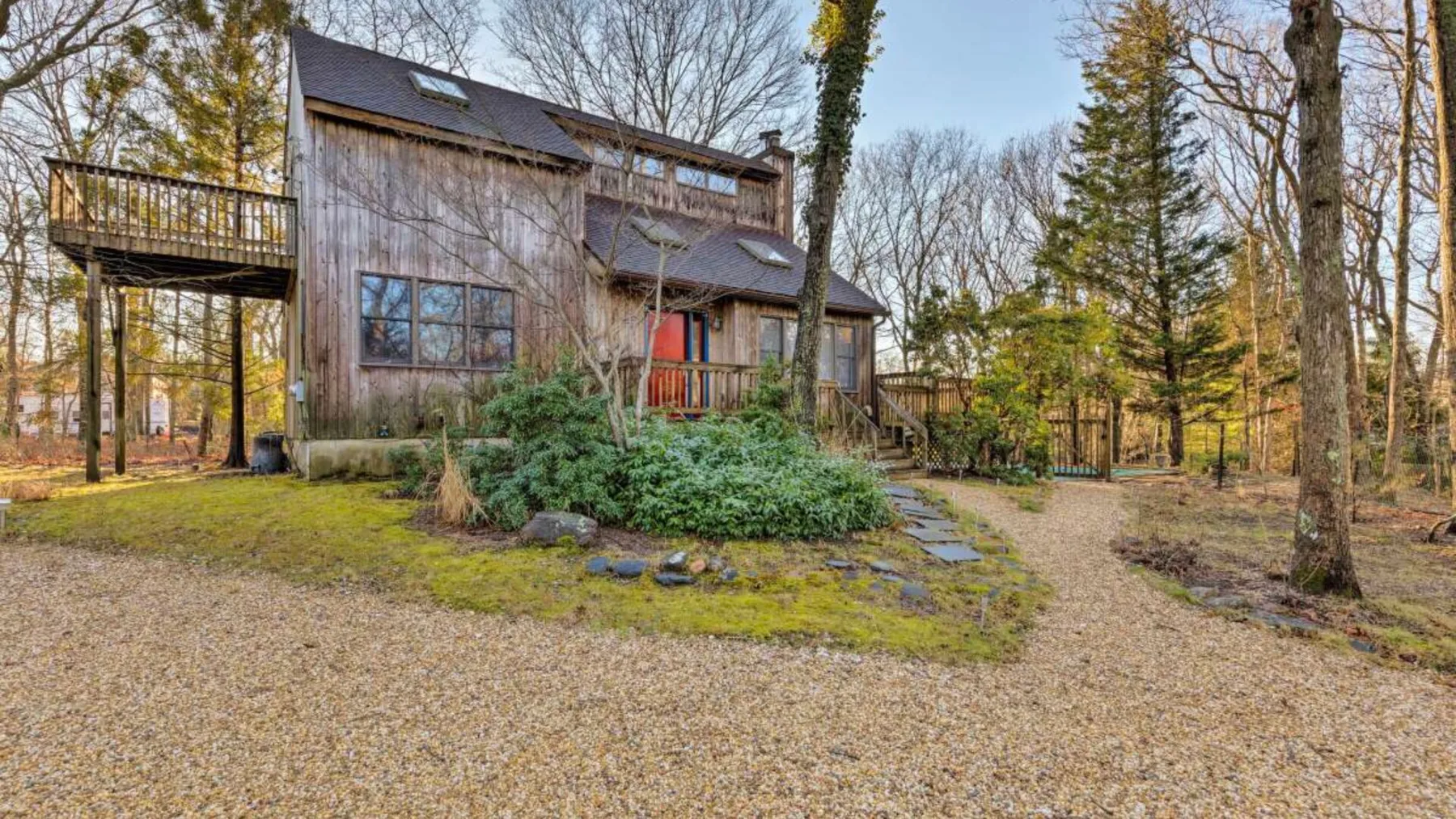 A wooded yard surrounds a two-story house with a raised deck.