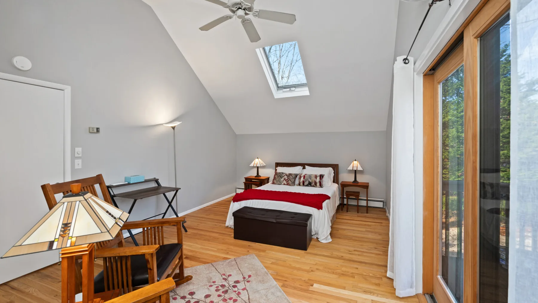 A bright bedroom with a bed, skylight, and large glass doors.