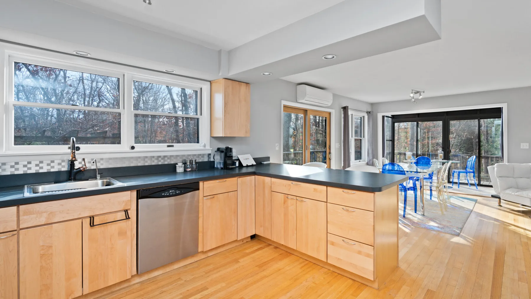 A bright open-plan kitchen with wooden cabinets and a dining area by large windows.