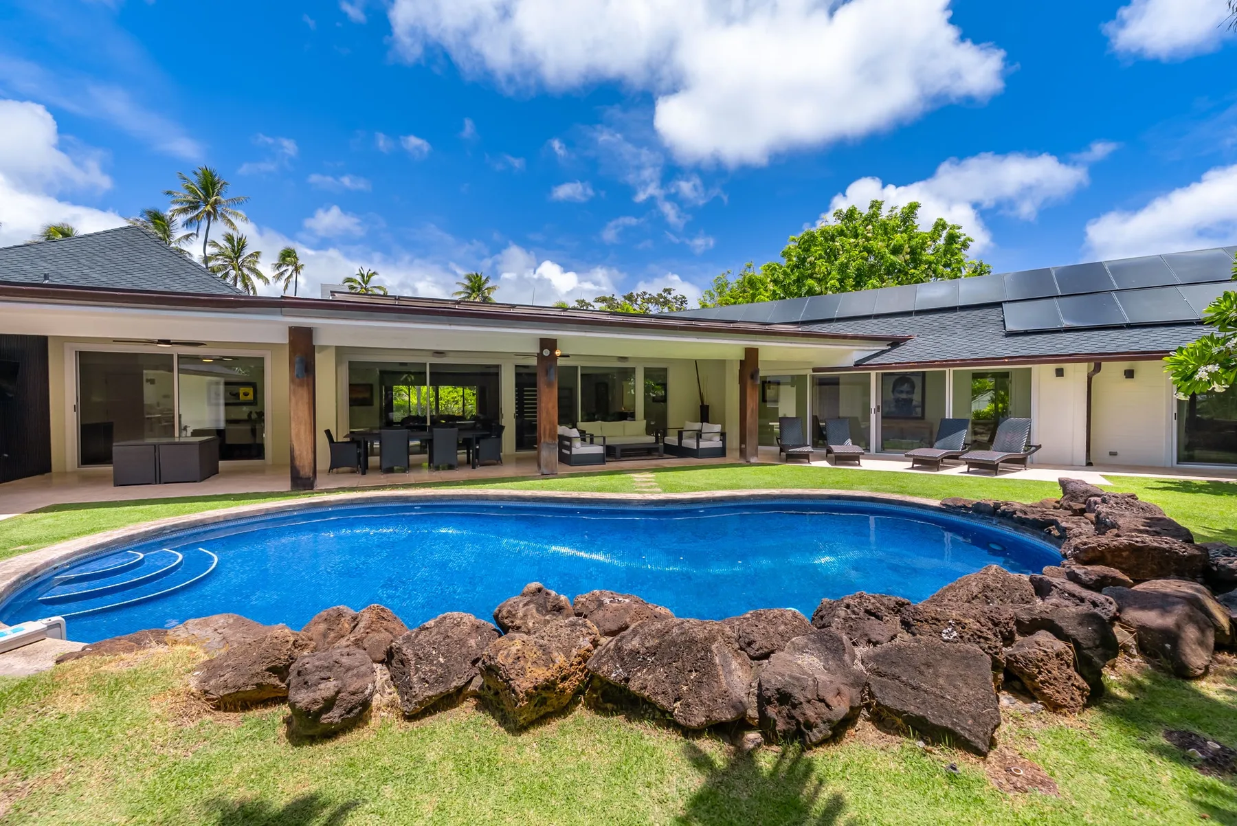 Una piscina exterior curva se encuentra frente a una casa de una planta.