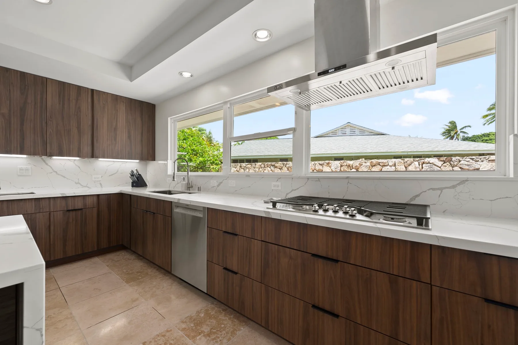 Una cocina moderna con gabinetes de madera oscura y una encimera larga bajo ventanas amplias.