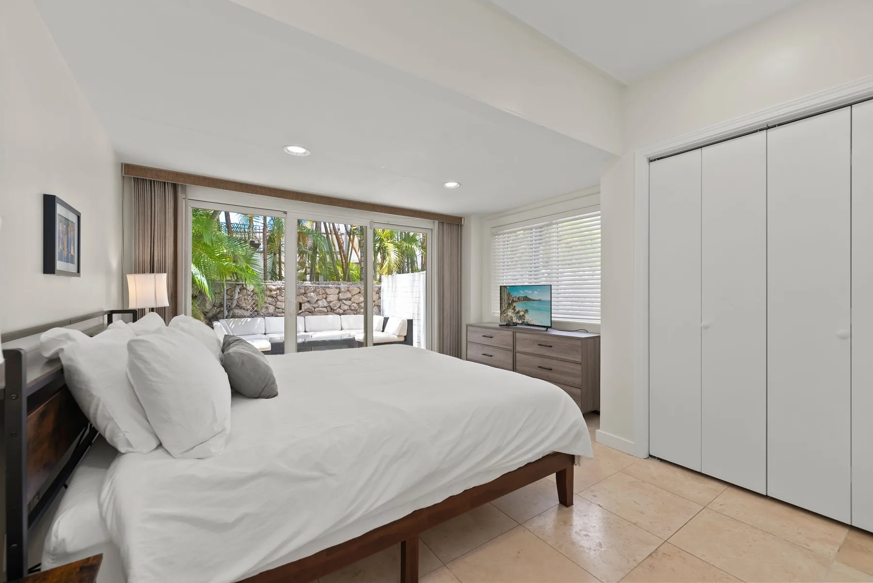 Un dormitorio con una cama grande, puertas corredizas de vidrio y una vista frondosa al exterior.