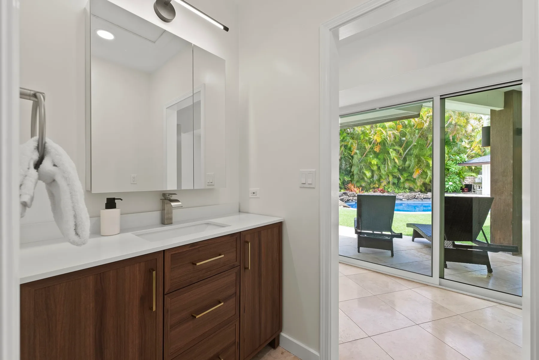 Un tocador de baño luminoso da a un patio con piscina y vegetación.