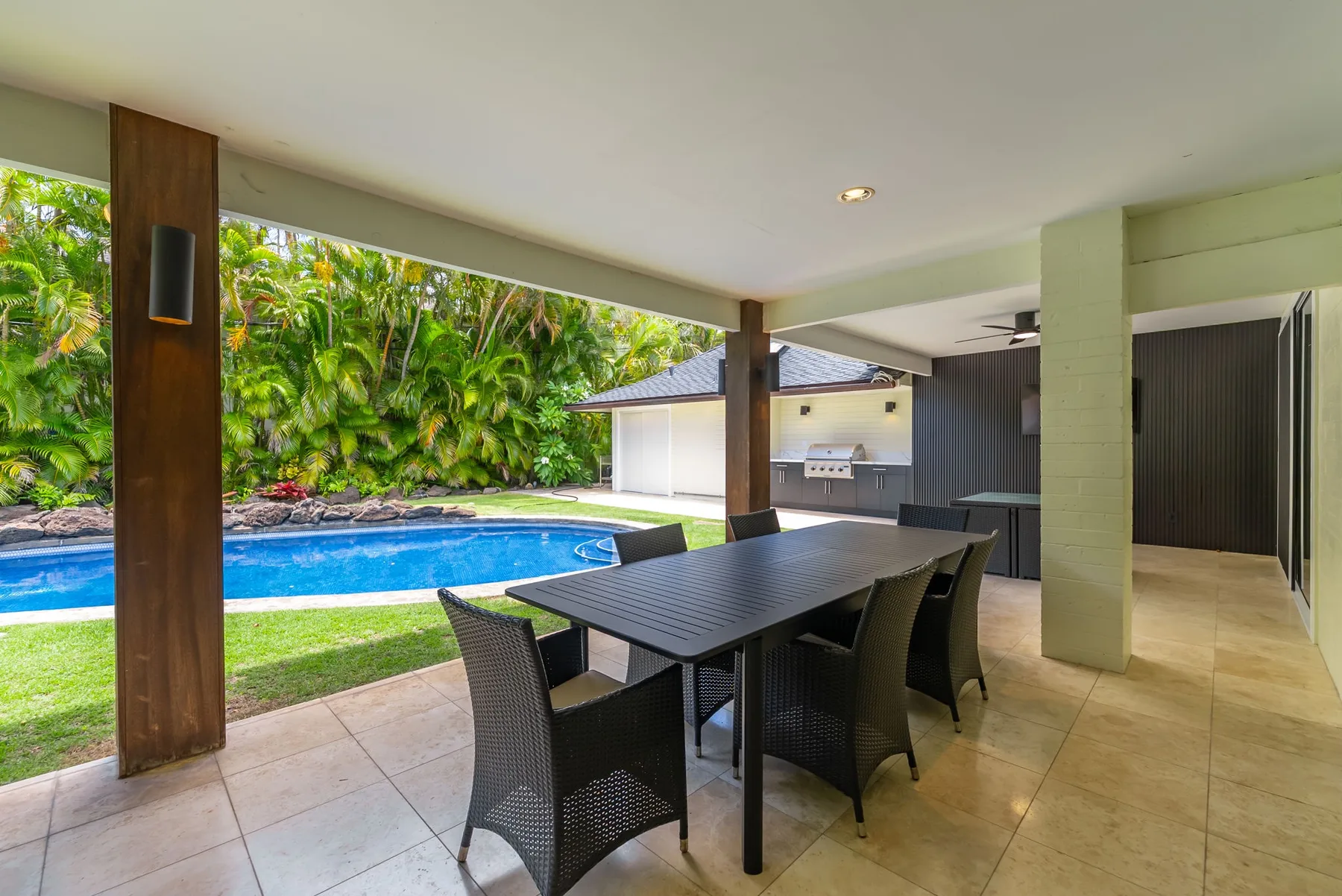 A covered patio dining area overlooks a swimming pool and garden.