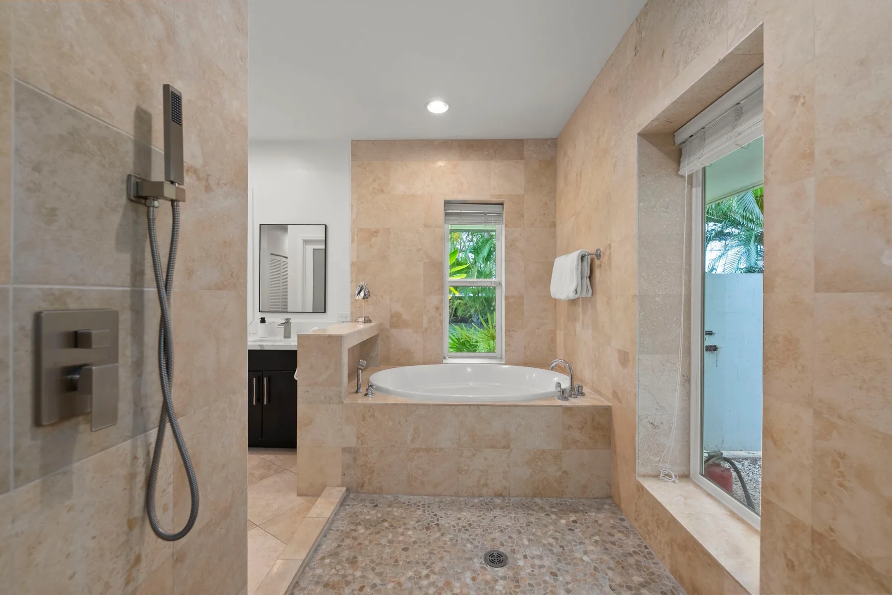 Un baño revestido de azulejos tiene una bañera bajo una ventana y una zona de ducha acristalada.