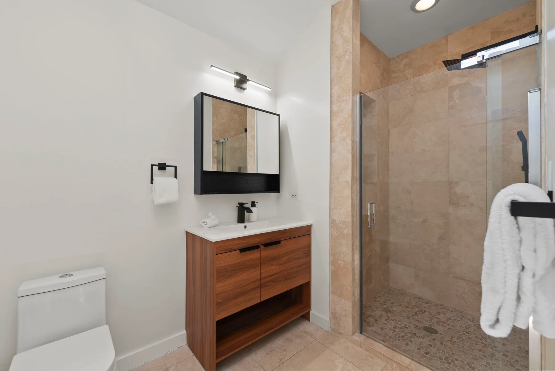 Un baño con un mueble de madera, espejo de pared y ducha de vidrio.