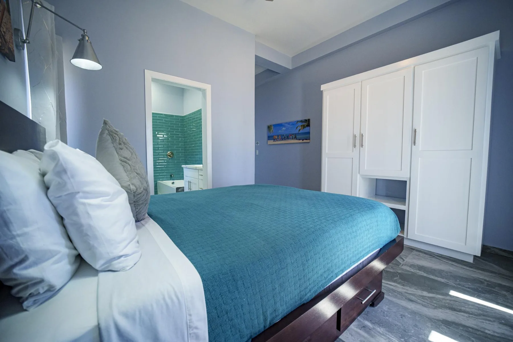A bedroom with a bed covered in a teal bedspread and a large white wardrobe.