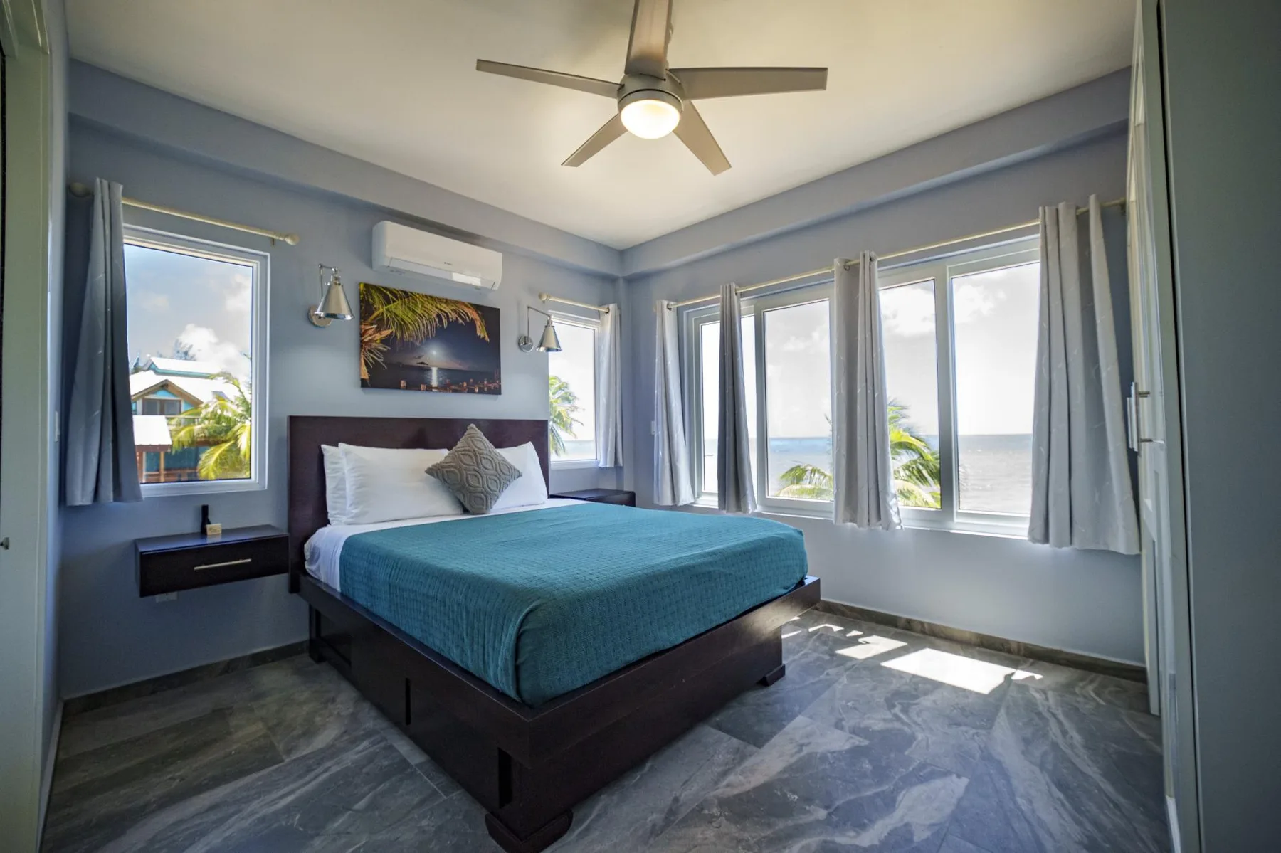 A bedroom with a bed beside several windows overlooking the water.