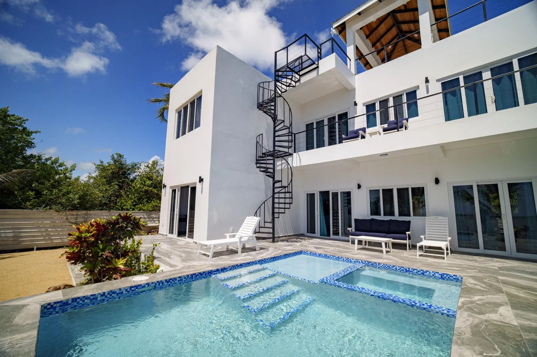 A modern white building overlooks a swimming pool and outdoor seating.
