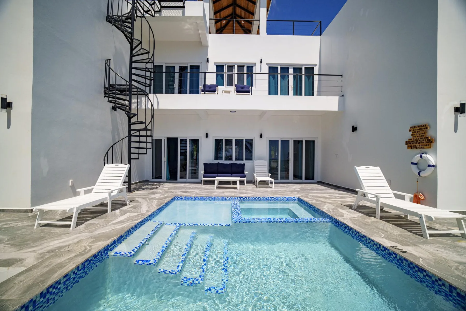 A courtyard swimming pool sits in front of a white multi-story building.