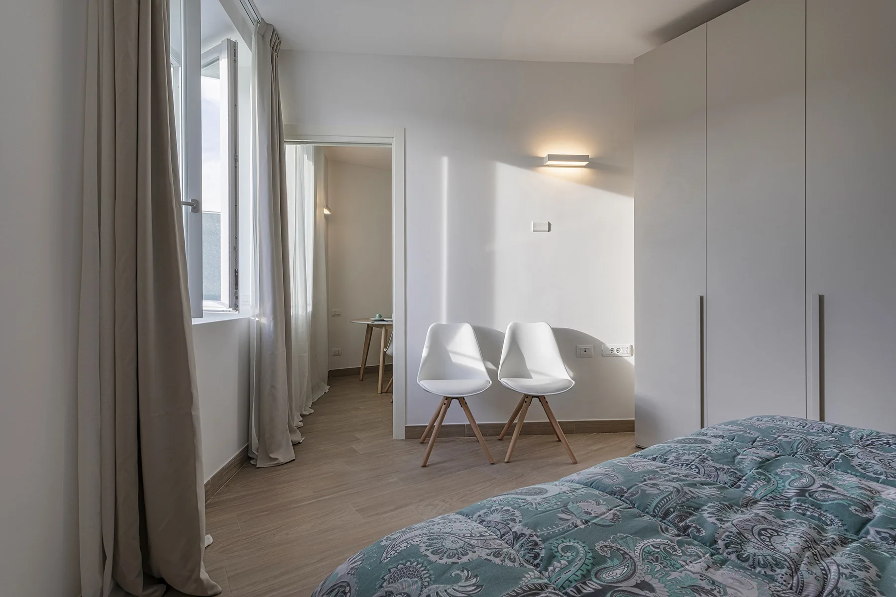 Un dormitorio con una cama, dos sillas y una ventana con cortinas.