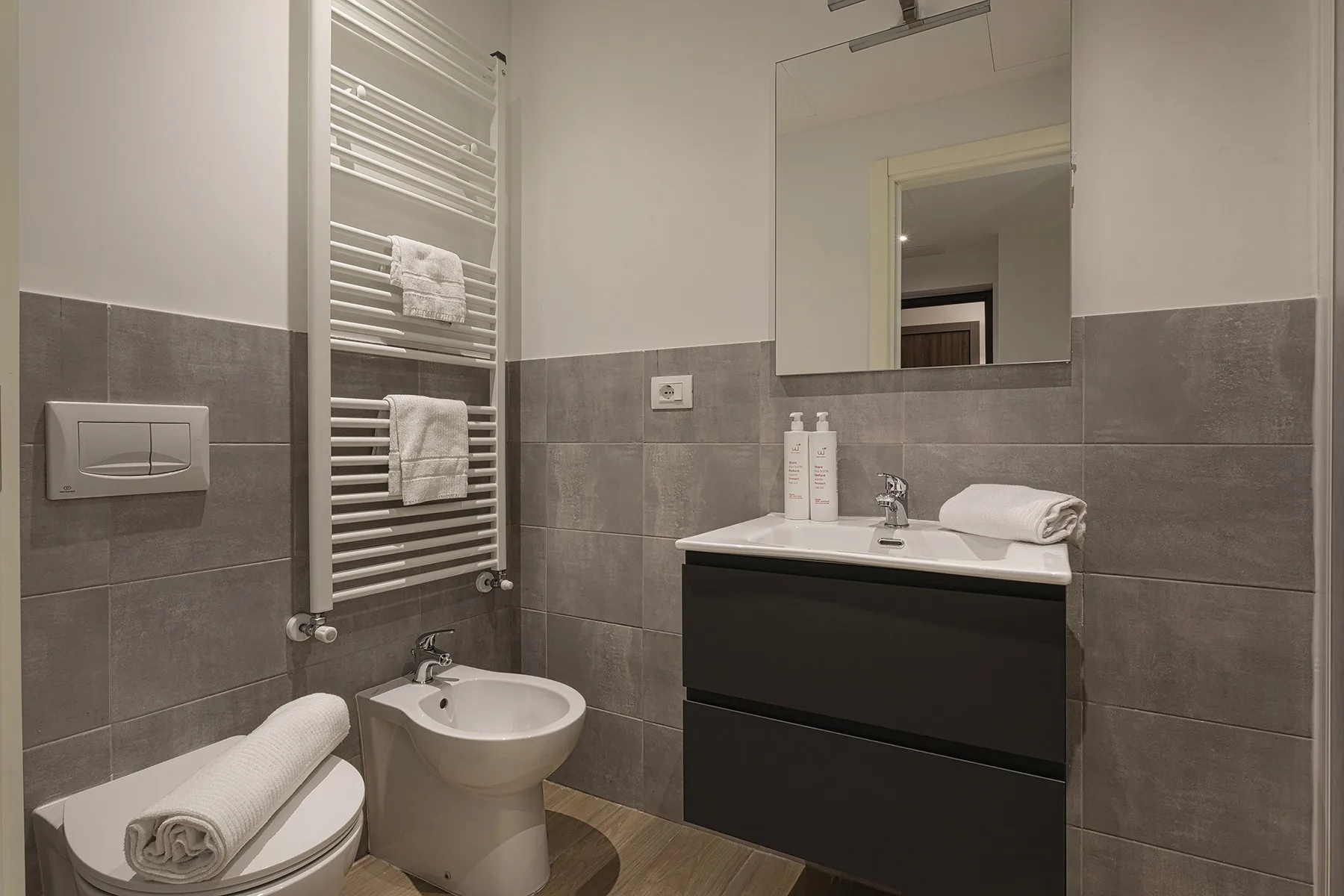Un baño con azulejos, lavabo, inodoro, bidé y toallero calefactor de pared.