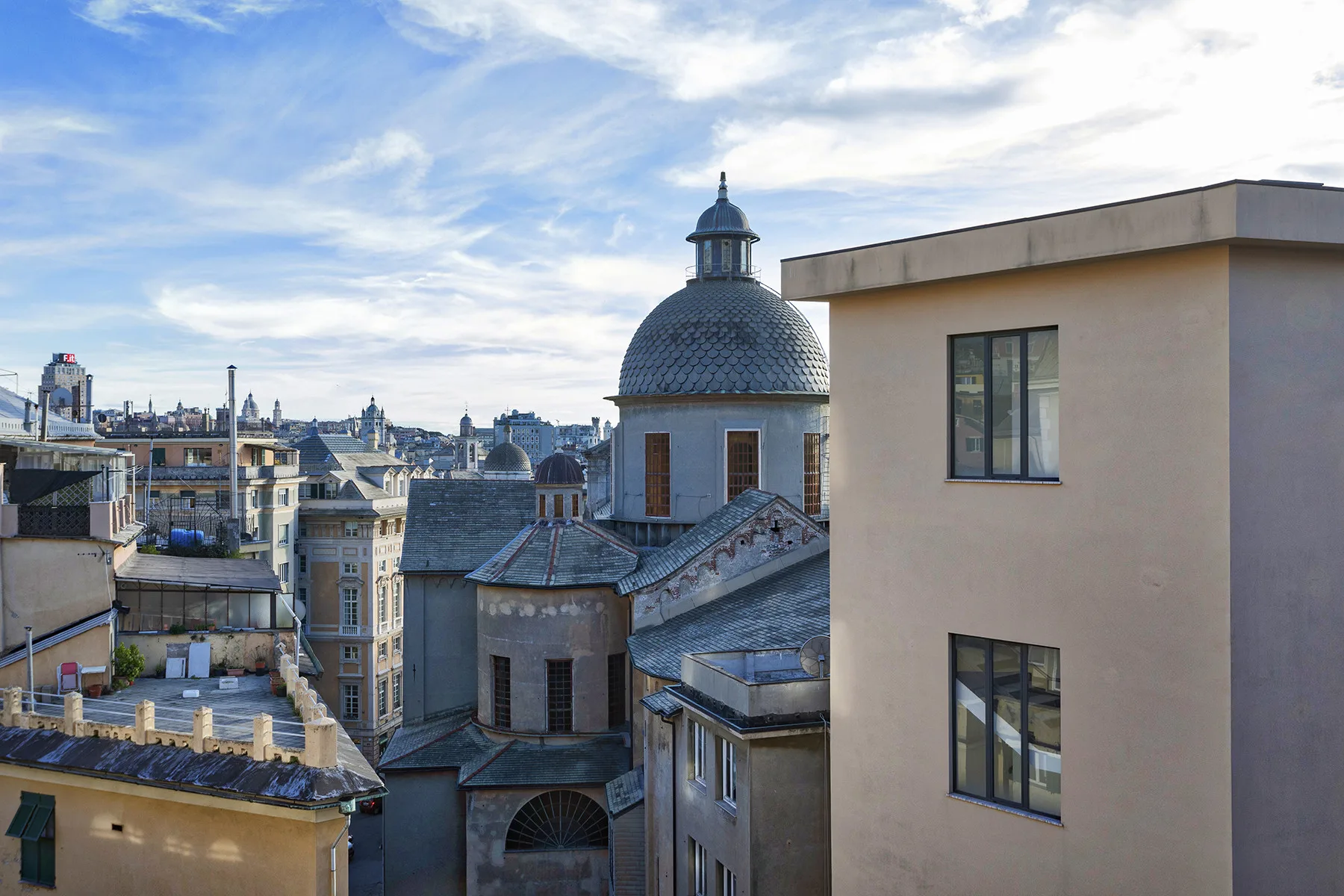 Los tejados y una torre con cúpula se alzan junto a un edificio moderno bajo un cielo parcialmente nublado.