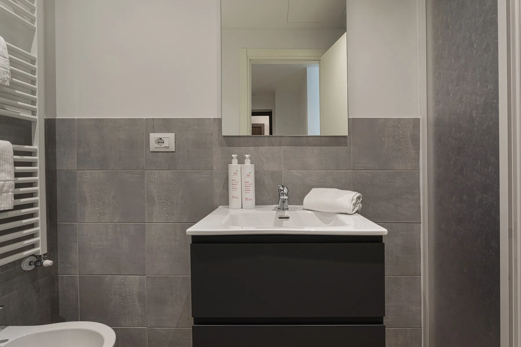 Un mueble de baño con lavabo, espejo y paredes de azulejos grises.