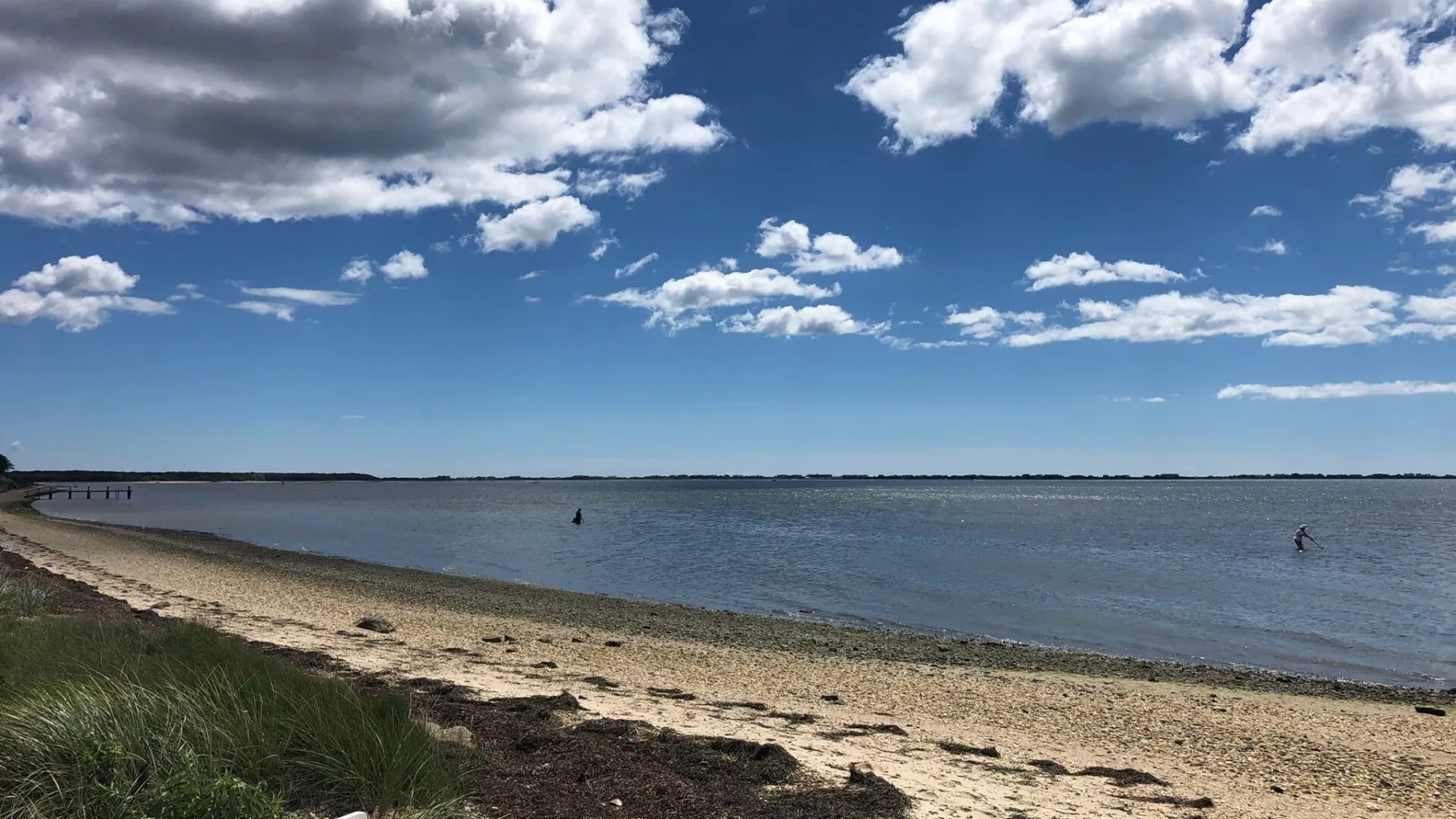 A sandy shoreline borders calm water beneath a partly cloudy sky.