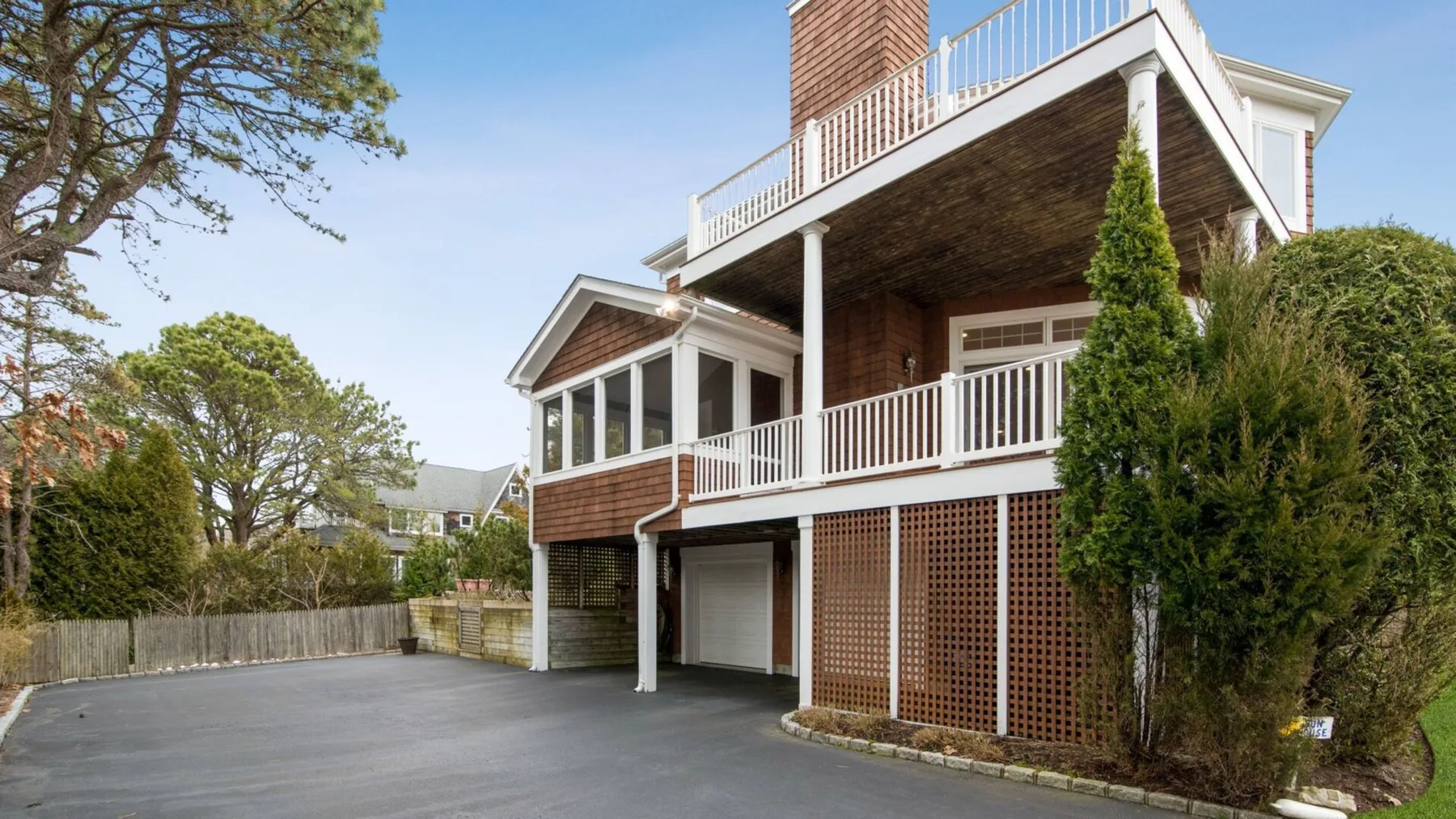 A multi-level house with white railings overlooks a paved driveway.