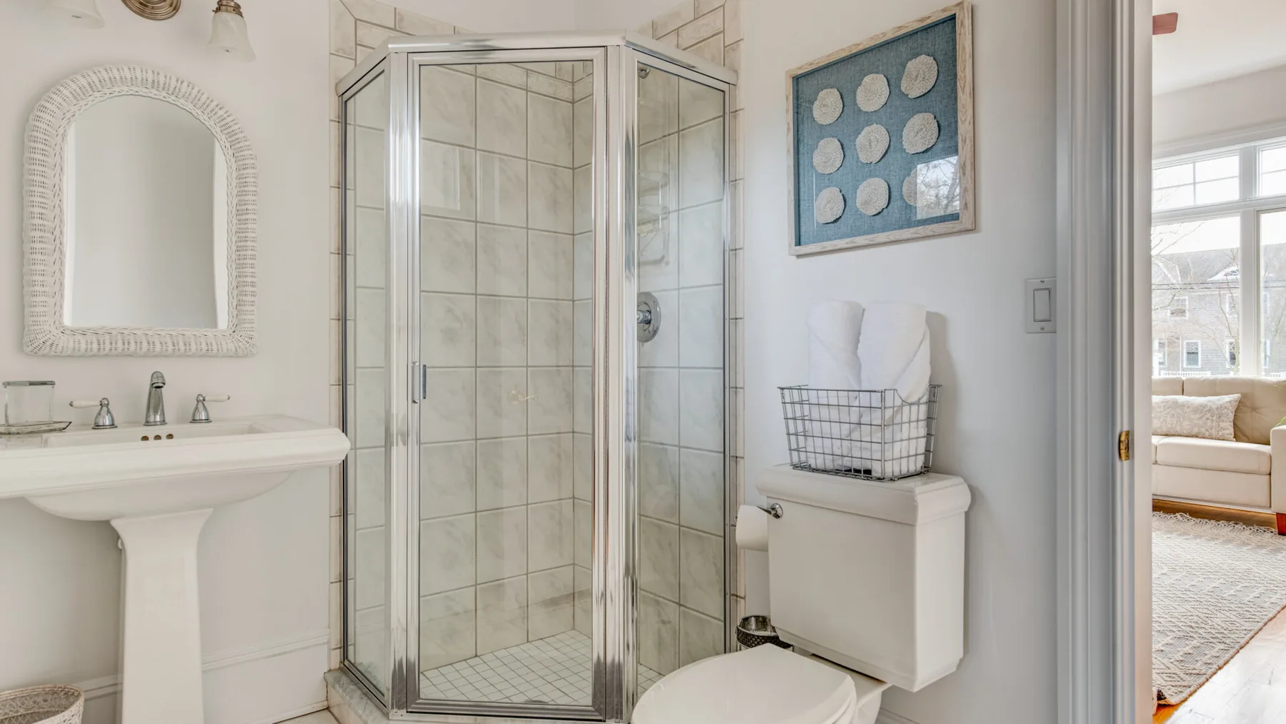 A bright bathroom with a tiled shower, pedestal sink, and toilet.