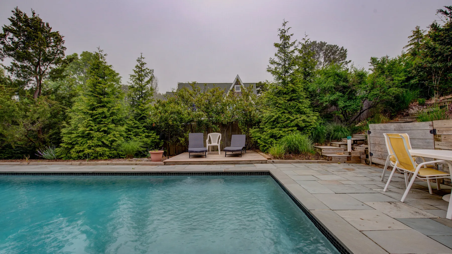An outdoor swimming pool sits beside a paved patio with seating.