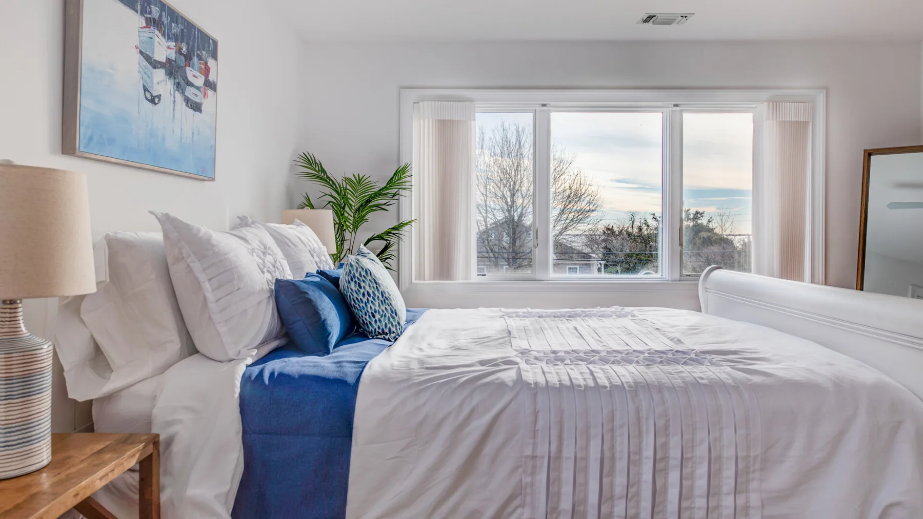 A bright bedroom with a neatly made bed and a large window.