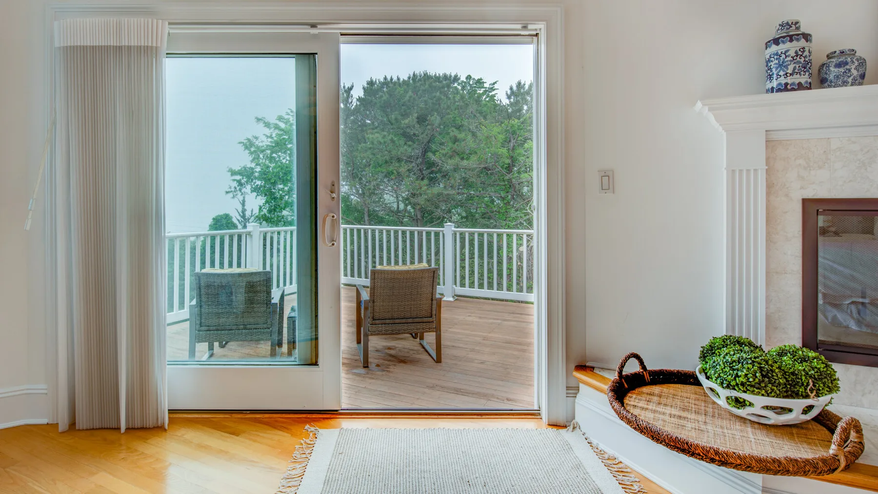 A bright living area opens through sliding glass doors to a deck with outdoor seating.