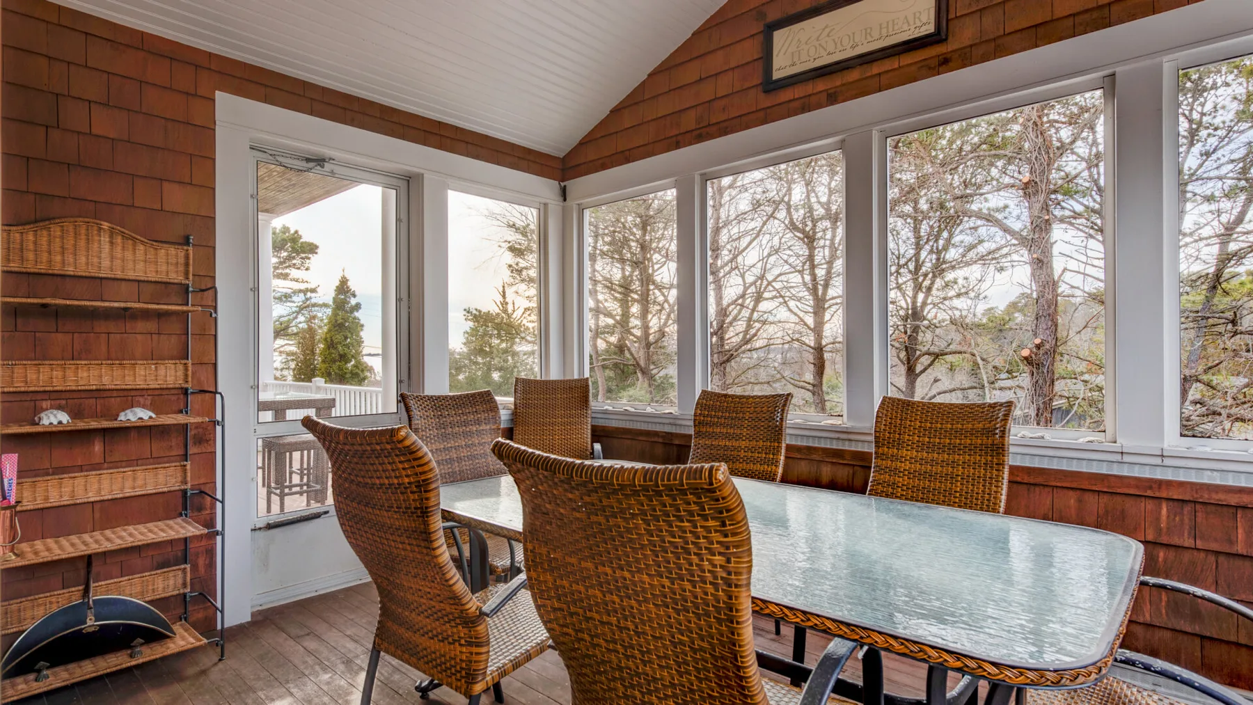 A sunroom with woven seating around a glass table and large windows.