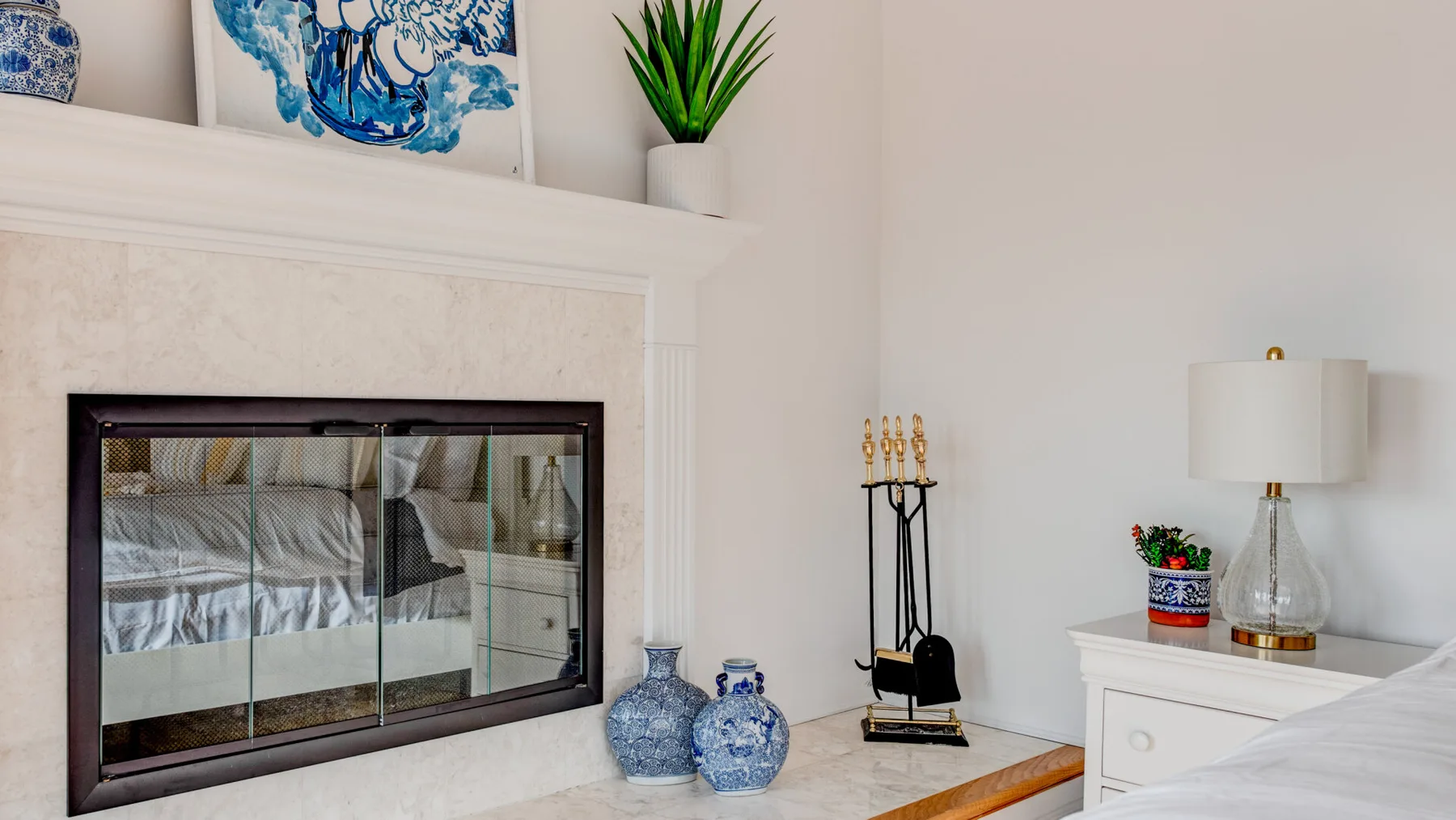 A living room fireplace sits beneath blue artwork, with decorative vases and a lamp nearby.