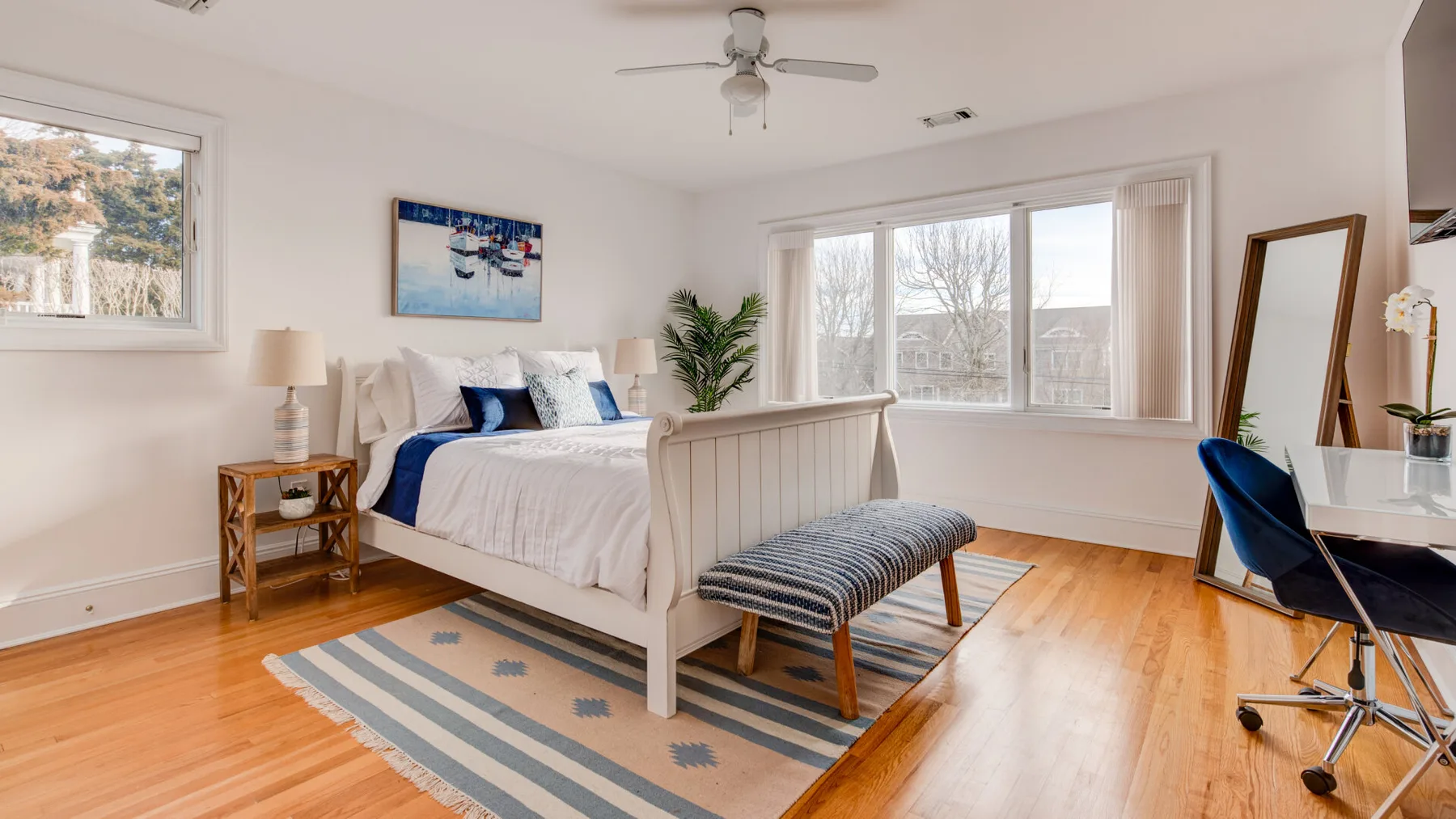 A bright bedroom with a bed, large windows, and a ceiling fan.
