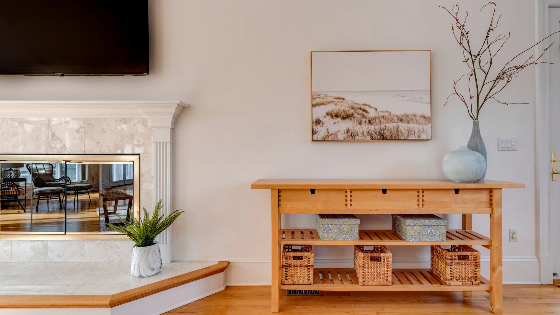A living room with a fireplace, wooden console, and framed landscape artwork.