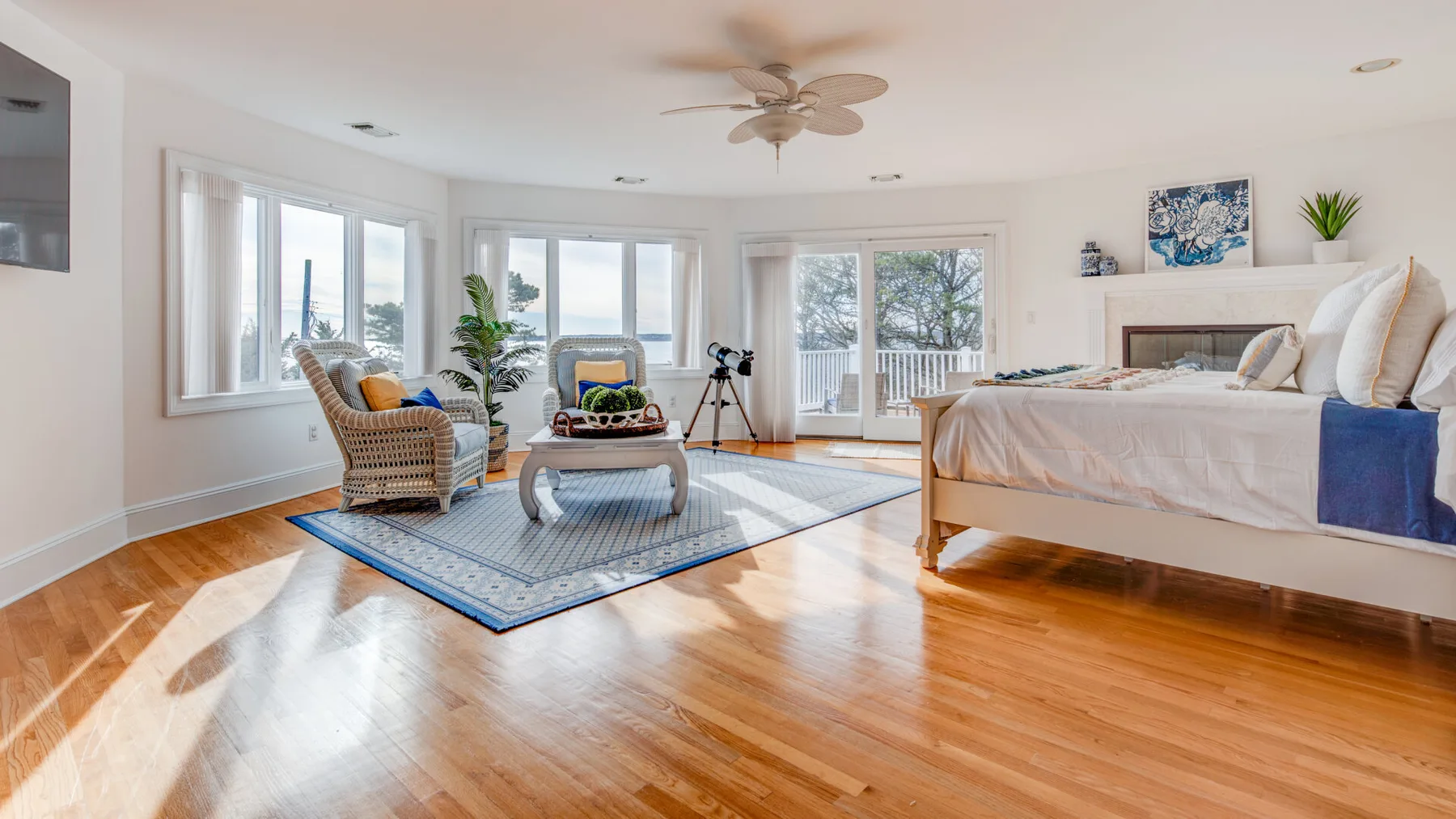 A bright bedroom with a seating area, large windows, and polished wood flooring.