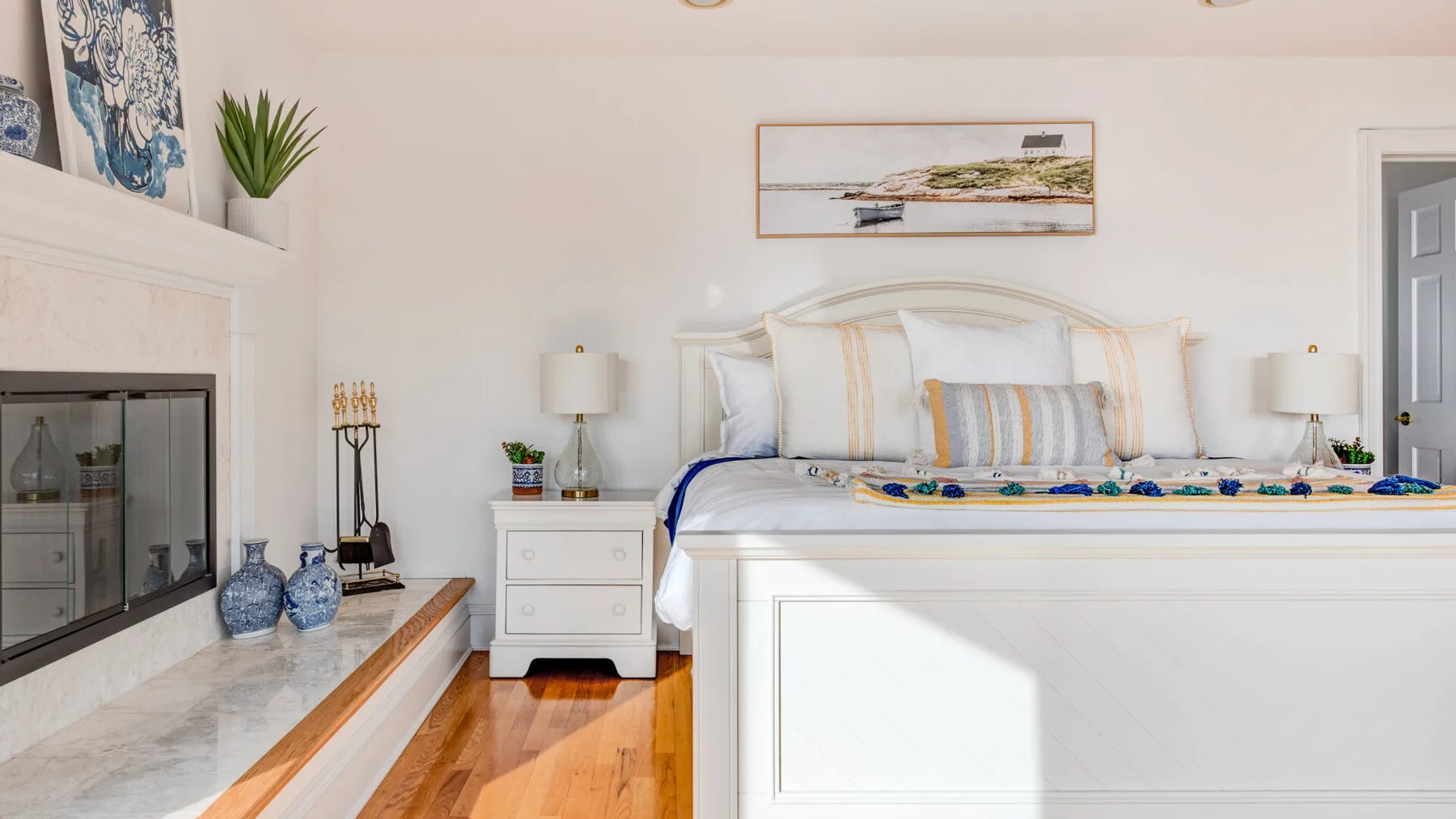 A bright bedroom with a bed, bedside tables, and a fireplace.