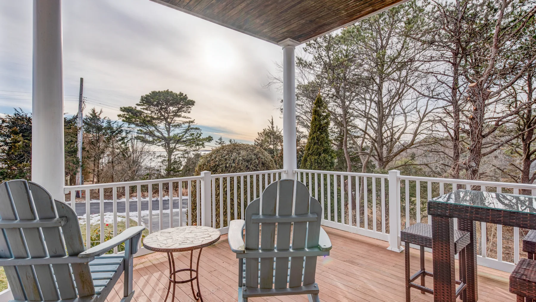 A covered outdoor deck with seating overlooks trees and a cloudy sky.