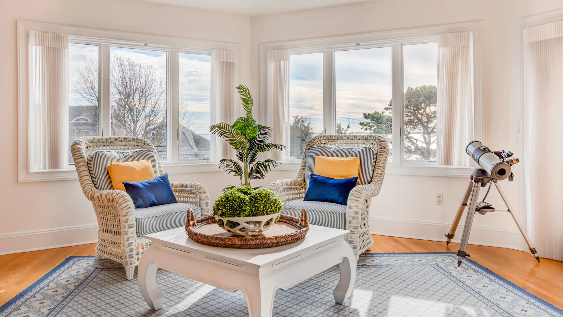 A bright sitting area has wicker seating, a coffee table, and wide windows.