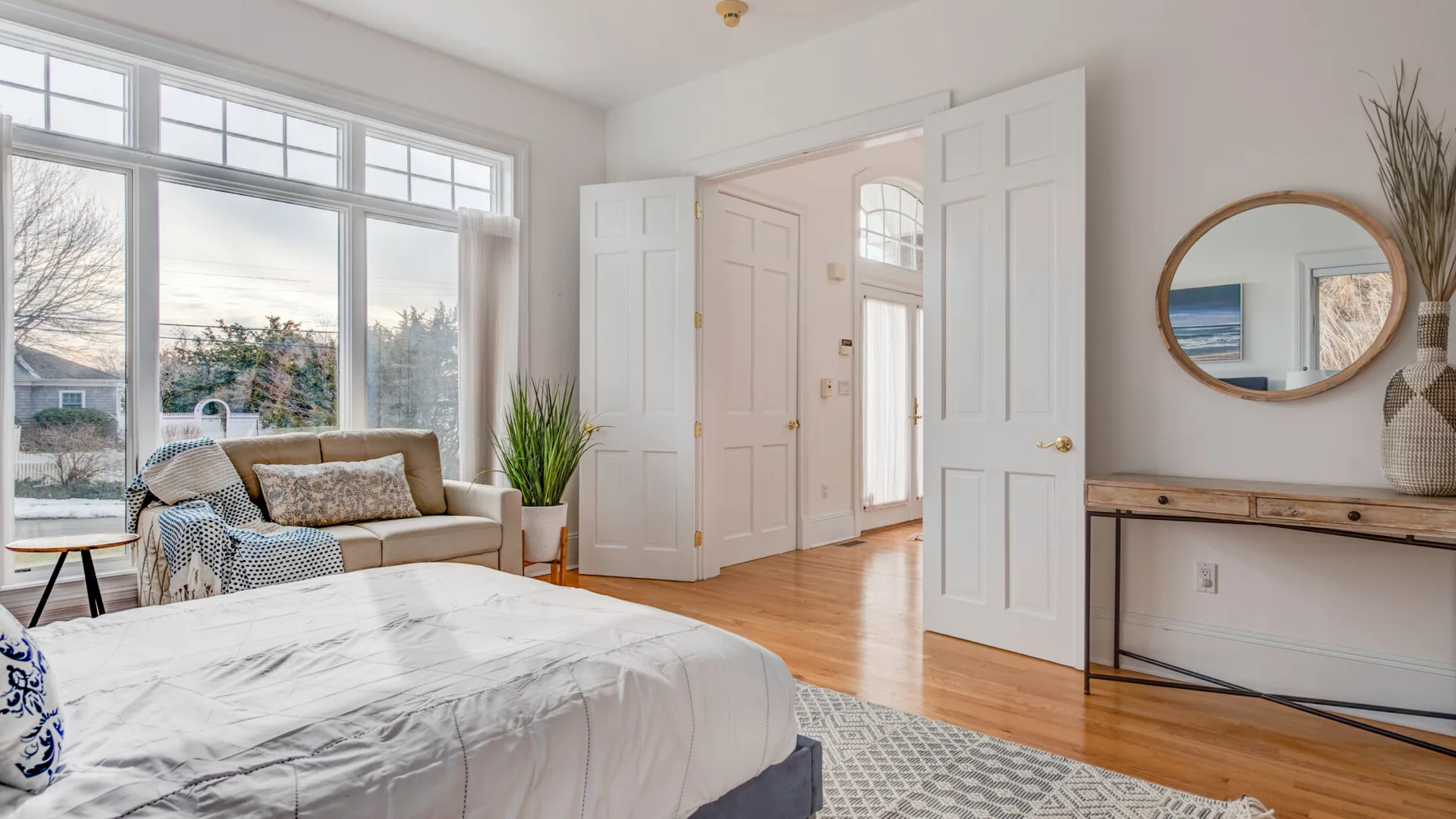 A bright bedroom with a large bed, tall windows, and open double doors.