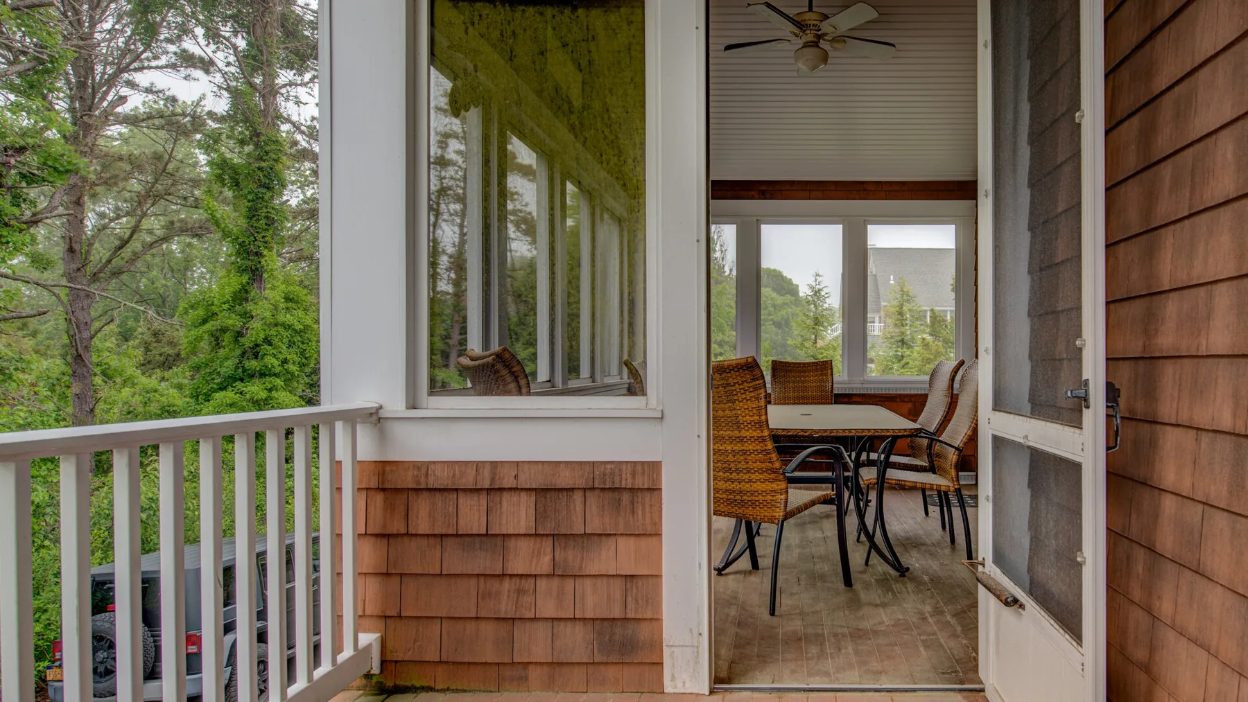A screened porch with a dining table and chairs beside large windows.