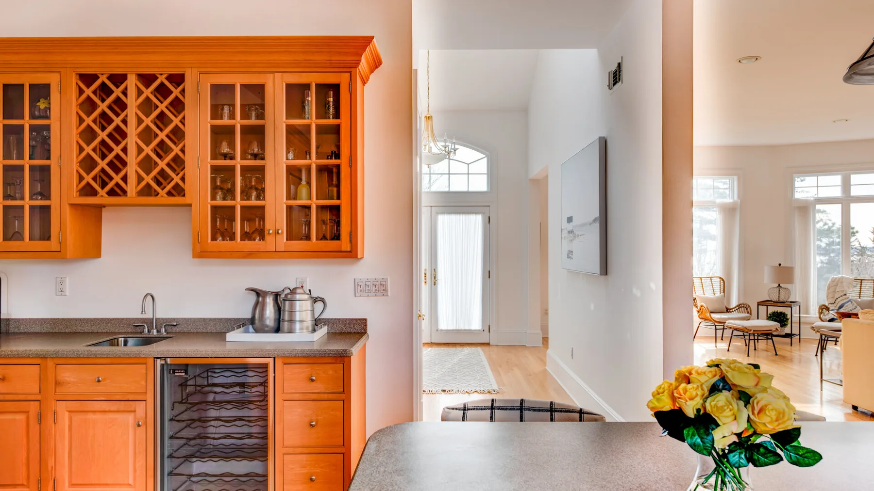A kitchen with wooden cabinets and a counter opens onto a bright living area.