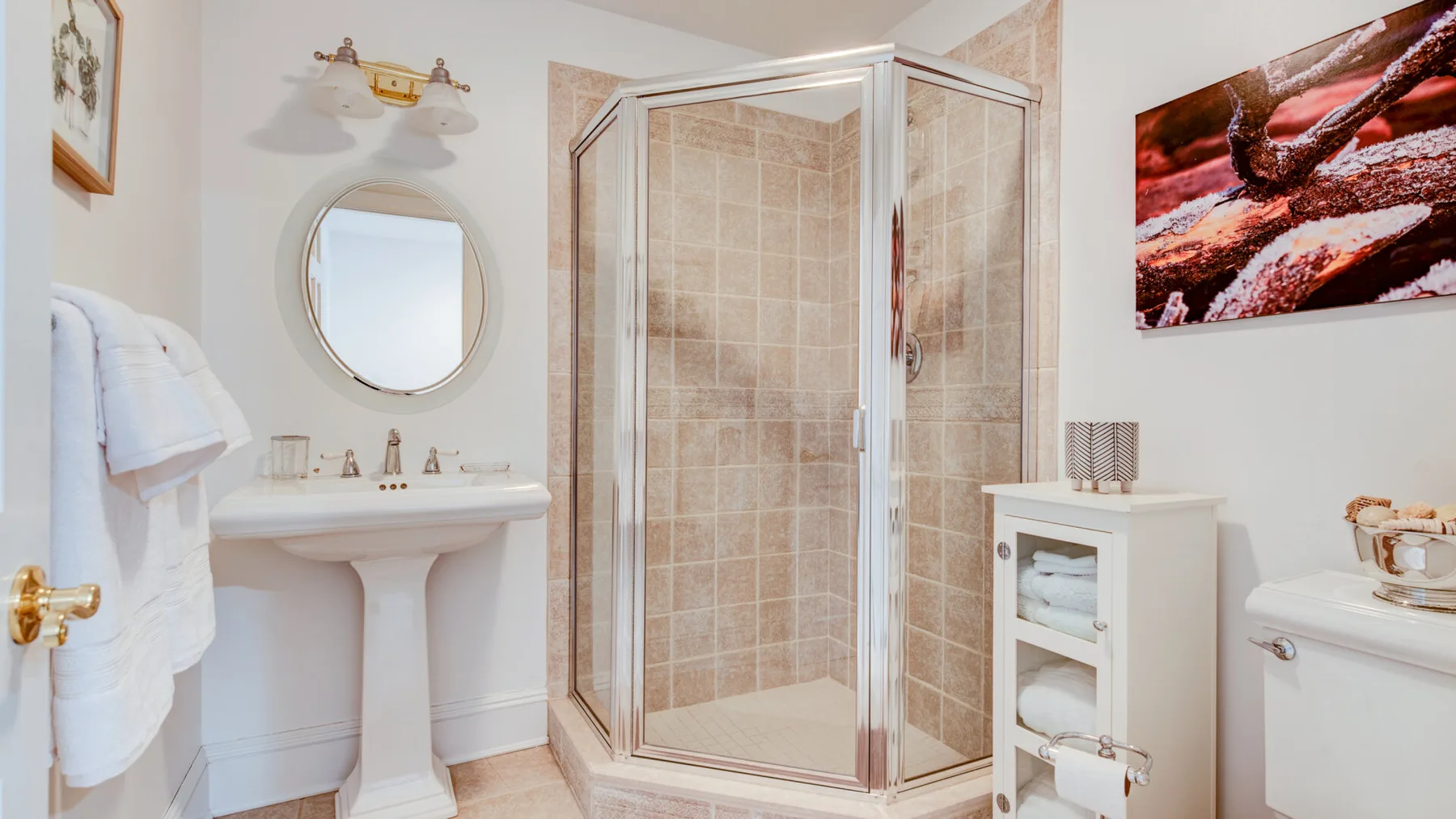 A bathroom with a glass shower, a sink, and a round mirror.