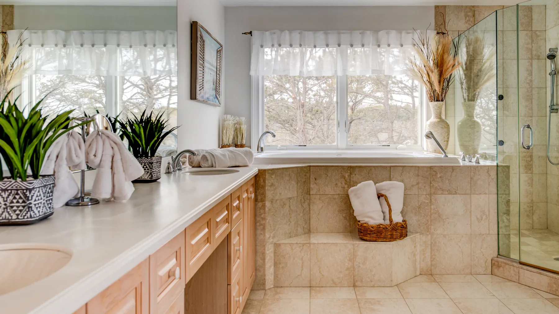 A bright bathroom with a bathtub beneath a large window and a glass shower.
