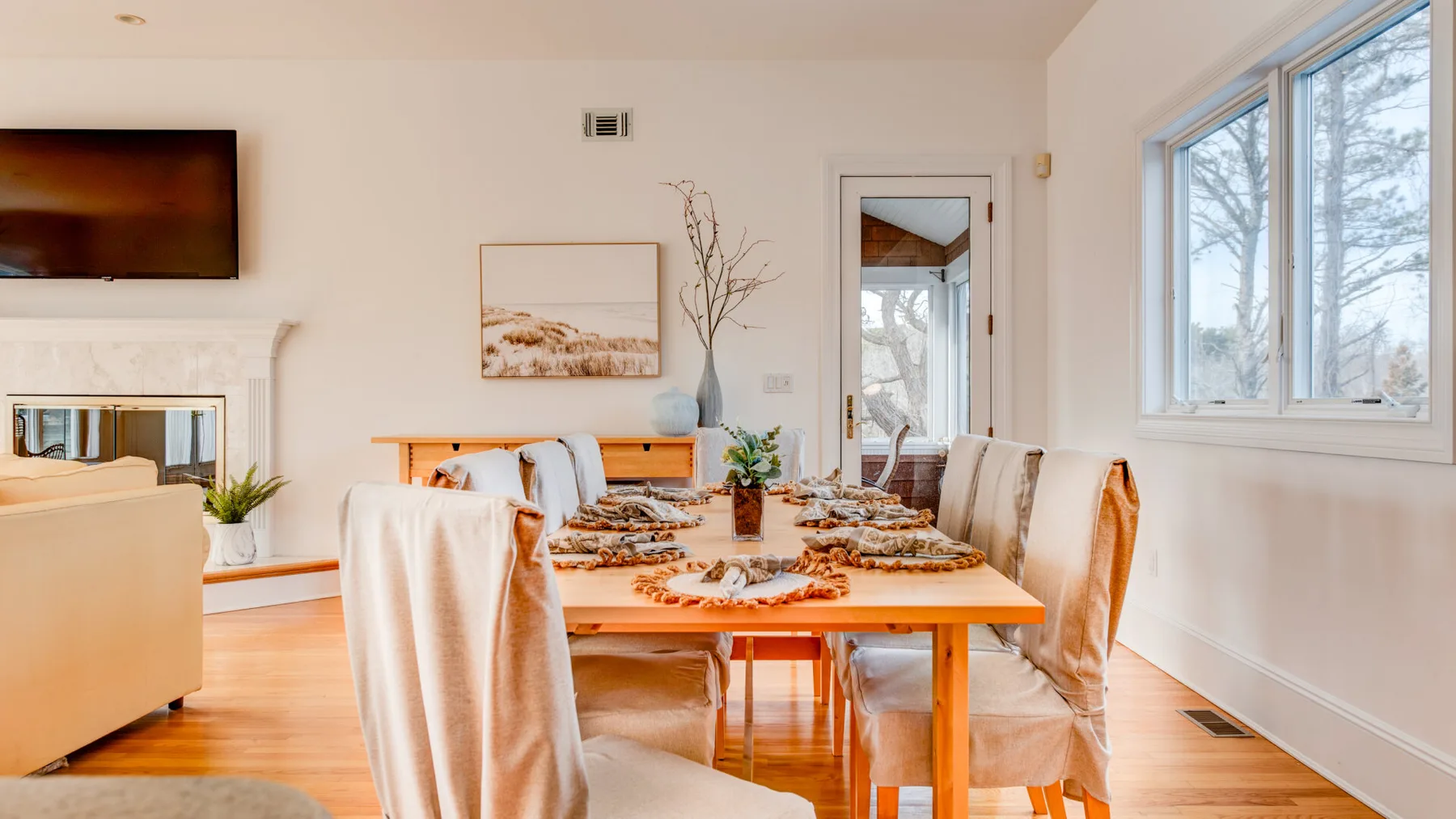 A dining area with a long table set for a meal beside large windows.