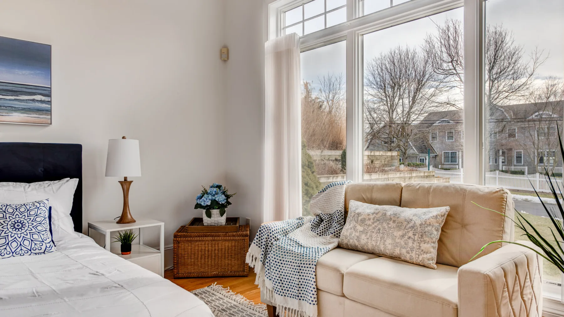 A bright bedroom with a bed beside a large window and seating.