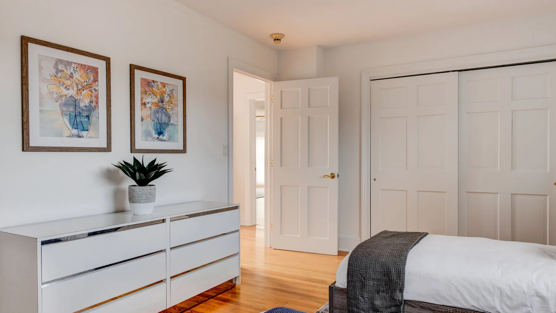 A bedroom with a bed, a dresser, and framed floral artwork.