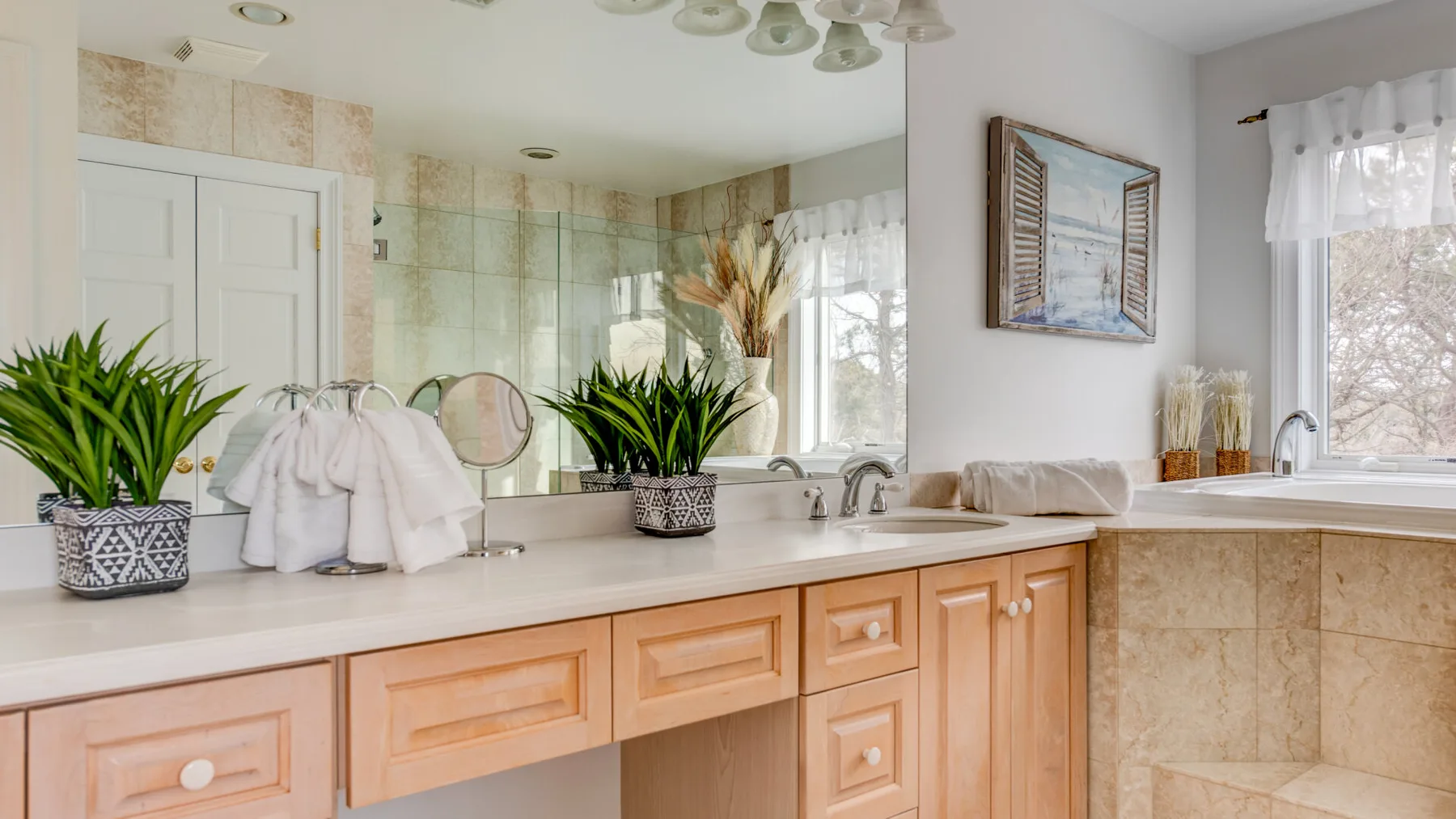 A bright bathroom vanity with a wide countertop, wooden cabinets, and a large mirror.