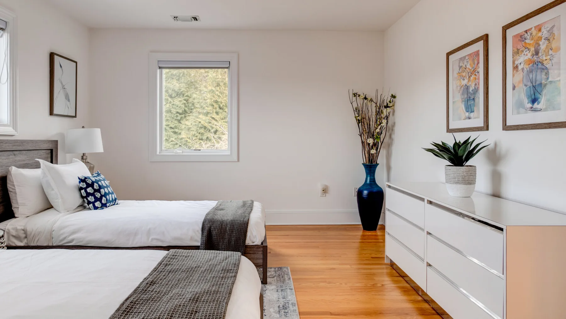A bright bedroom with beds, a dresser, and framed artwork.