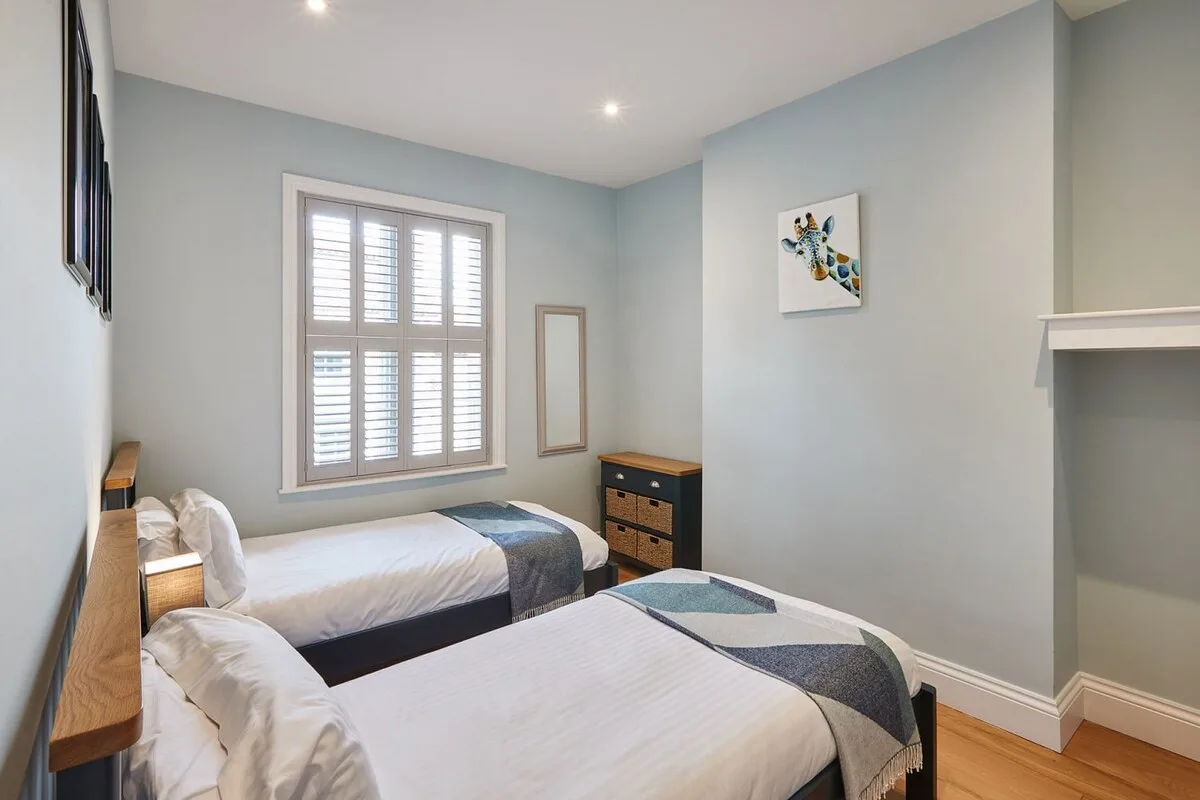Un dormitorio con dos camas, una ventana con contraventanas y una cómoda.
